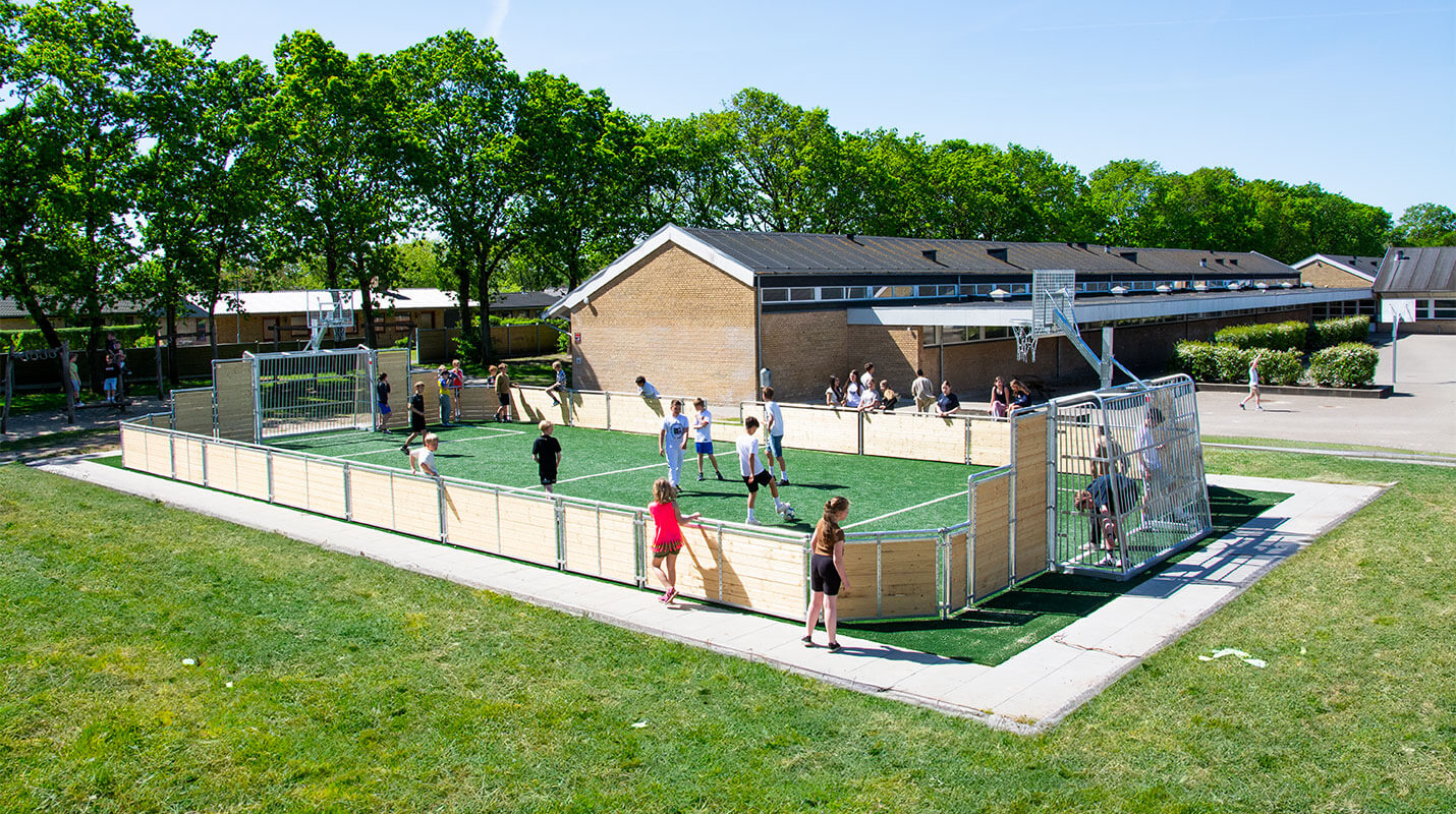 Børn spiller fodbold på en multibane i gran med kunstgræs i skolegården på Brårup Skole.