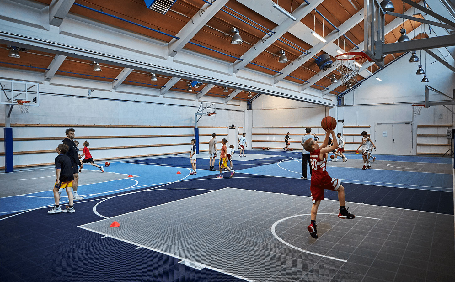 Idrætshal med basketstativer, hvor børnene træner og spiller basketball