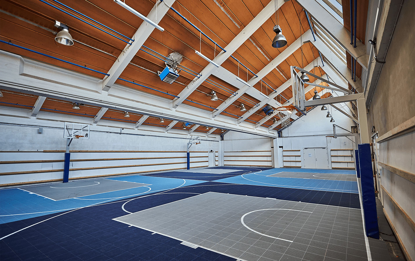 En ny idrætshal med flere basketstativer og underlag af blå-grå PP-fliser