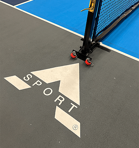 Hvidt A-Sport-logo på gulvet på en True Court indendørs pickleballbane og pickleball-konkurrencenet med transporthjul.