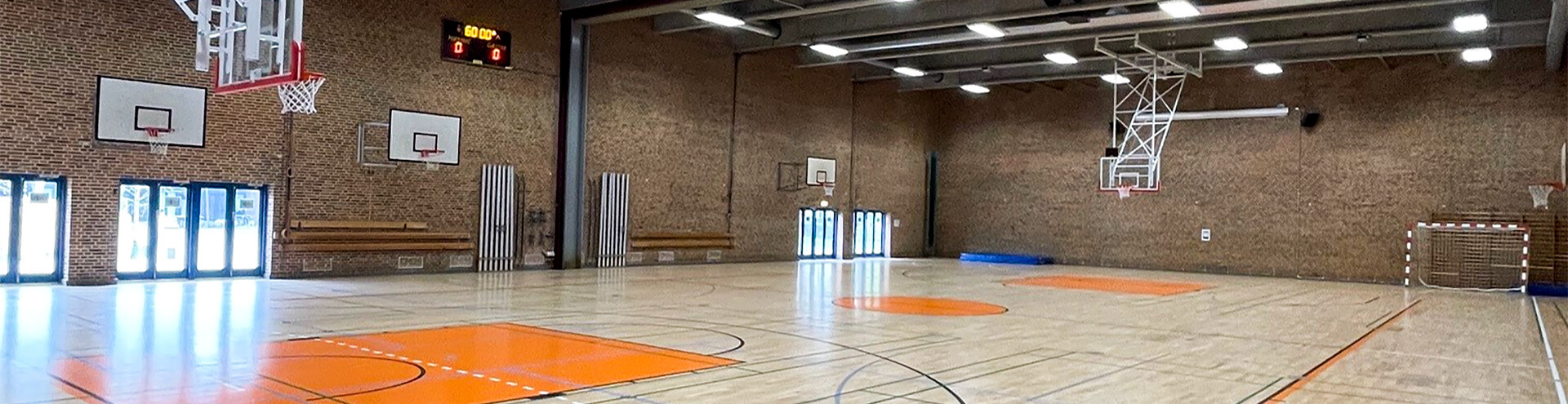 Loftmonterede motorbasketstativer og gulvopstregning af basketballbane i hallen.