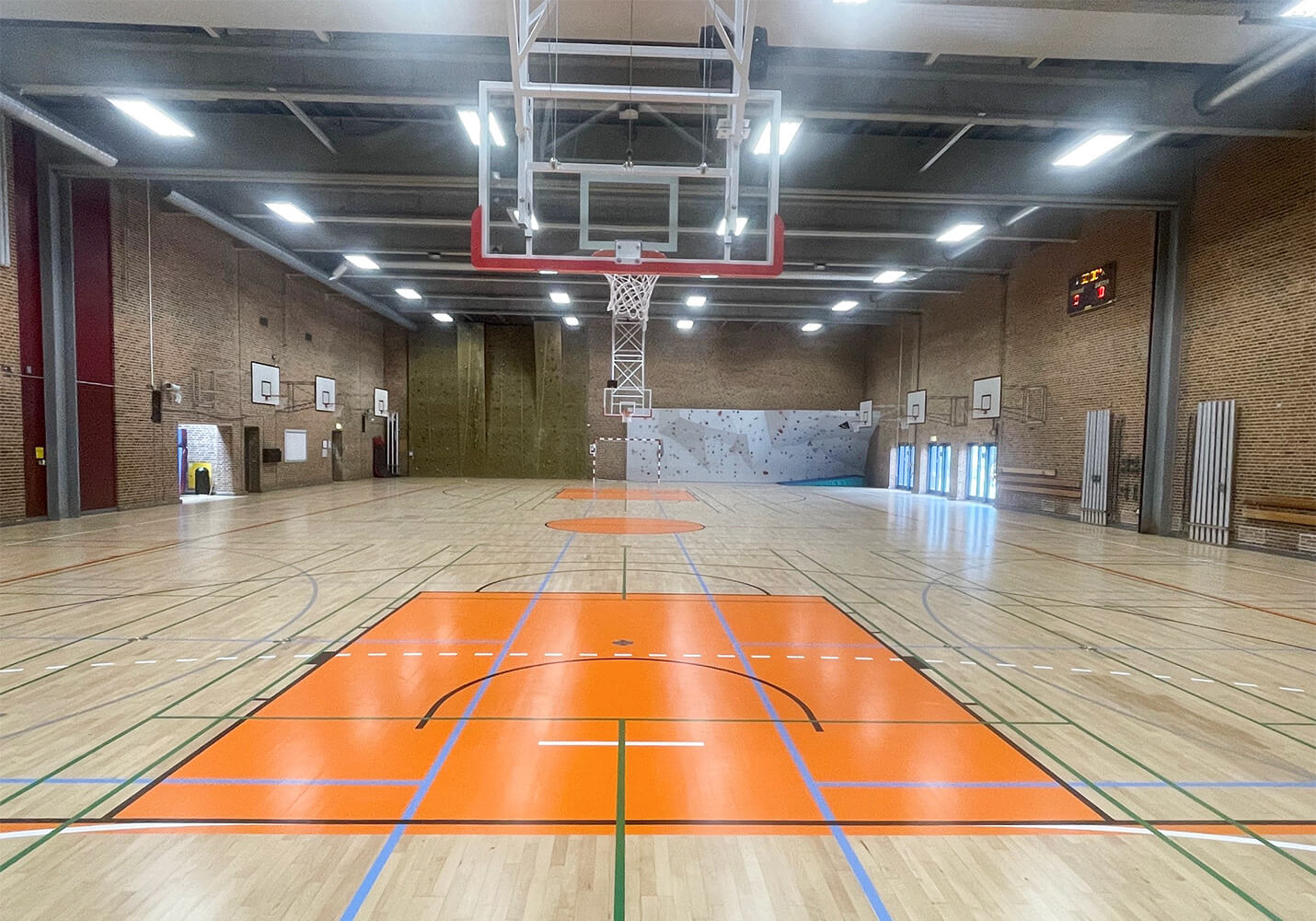 Loftmonterede motorbasketstativer og gulvopstregning af basketballbane i hallen.