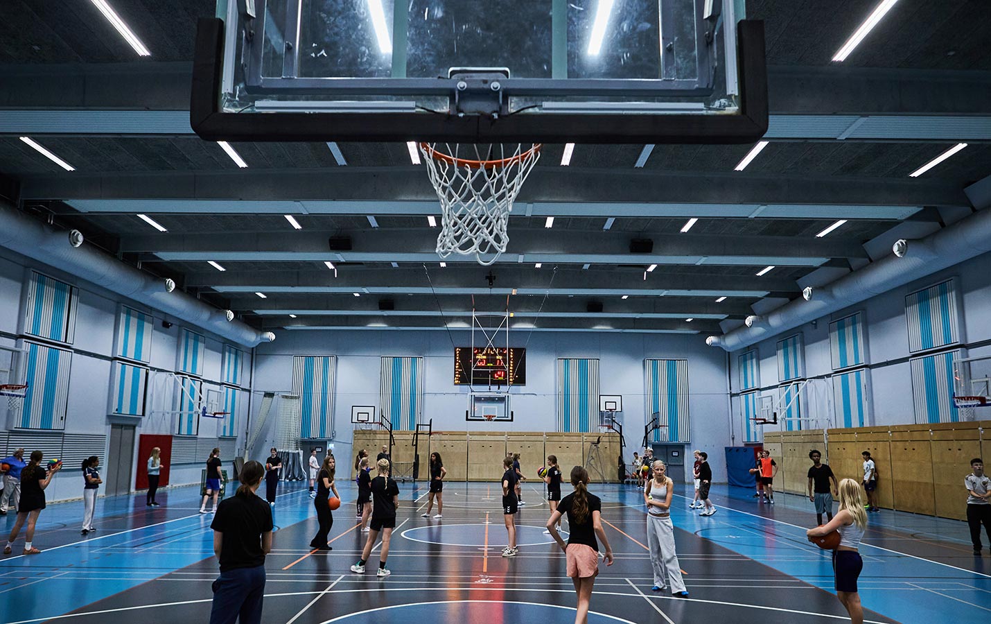 Elever spiller basketball i hallen med stor scoringstavle